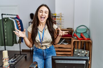 Young brunette woman working as manager at retail boutique celebrating mad and crazy for success with arms raised and closed eyes screaming excited. winner concept