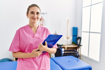 Young blonde woman wearing physiotherapist uniform working at physiotherapy clinic