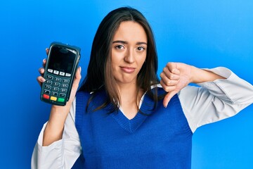 Young hispanic girl holding dataphone with angry face, negative sign showing dislike with thumbs...
