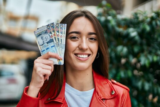 Young hispanic woman smiling happy holding peruvian sol banknotes at the city.