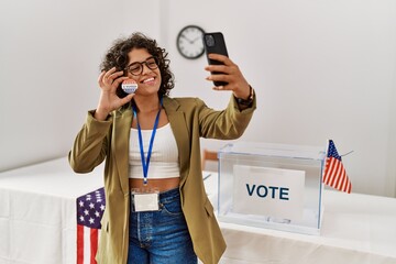 Young hispanic woman holding i voted badge make selfie by the smartphone at electoral college