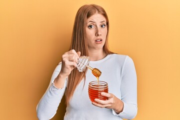 Young irish woman holding honey clueless and confused expression. doubt concept.