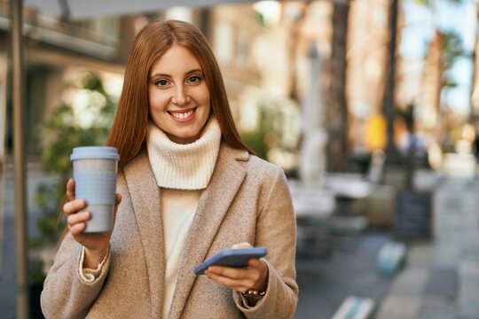 Young redhead girl using smartphone drinking coffee at the city.