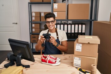 Young hispanic man ecommerce business worker make photo to sneakers at office