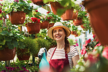 Woman gardener in hat and gloves works with flowers in the greenhouse. © Aleksandr Rybalko