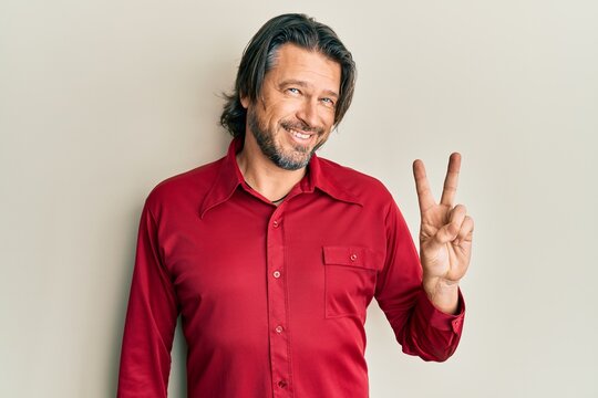 Middle age handsome man wearing casual clothes smiling with happy face winking at the camera doing victory sign. number two.
