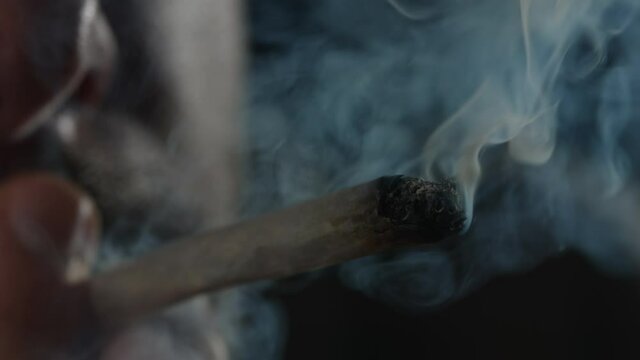 Male face silhouette with a burning cannabis joint, in a smoke cloud, on a black background, close-up shot.