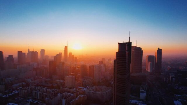 Morning flight over Warsaw. Aerial sunrise and fog oover Warsaw downtown skyline with skyscrapers, Poland. Reflections of the sun in the glass of a skyscraper