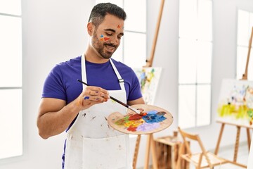 Young hispanic man smiling confident mixing color on palette at art studio