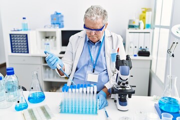 Middle age grey-haired man wearing scientist uniform using pipette at laboratory