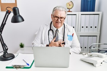 Senior caucasian man wearing doctor uniform and stethoscope at the clinic smiling and laughing hard out loud because funny crazy joke with hands on body.