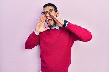 Hispanic man with beard wearing business shirt and glasses shouting angry out loud with hands over mouth