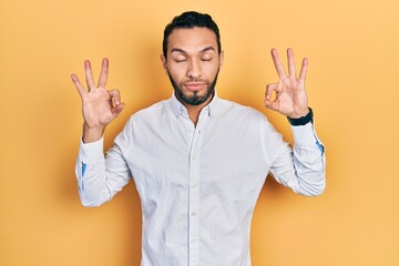 Fototapeta premium Hispanic man with beard wearing business shirt relax and smiling with eyes closed doing meditation gesture with fingers. yoga concept.
