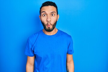Hispanic man with beard wearing casual blue t shirt making fish face with lips, crazy and comical gesture. funny expression.