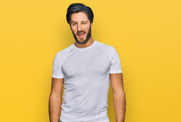 Young hispanic man wearing casual white t shirt winking looking at the camera with sexy expression, cheerful and happy face.