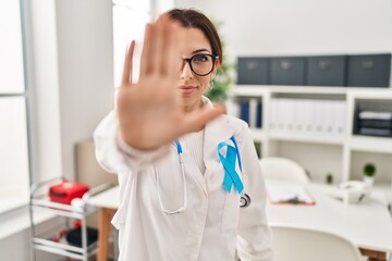 Young brunette doctor woman wearing stethoscope at the clinic doing stop sing with palm of the hand. warning expression with negative and serious gesture on the face.