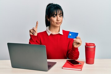 Young brunette woman with bangs working at the office using laptop and credit card smiling with an...