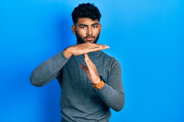 Arab man with beard wearing turtleneck sweater doing time out gesture with hands, frustrated and...