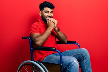 Arab man with beard sitting on wheelchair laughing nervous and excited with hands on chin looking to the side