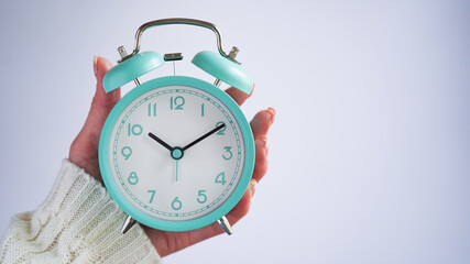 Close-up of woman hand holding blue retro alarm clock white background,time on clock is ten o'clock ten minutes,10:10.Time to wake up,early morning.Blue monday day concept.Copy space.Turquoise clock.