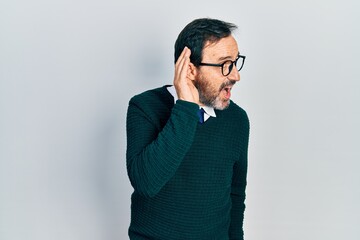 Middle age hispanic man wearing casual clothes and glasses smiling with hand over ear listening an hearing to rumor or gossip. deafness concept.