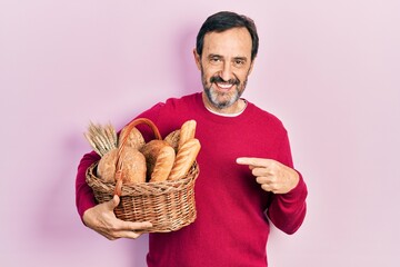 Middle age hispanic man holding wicker basket with bread smiling happy pointing with hand and finger