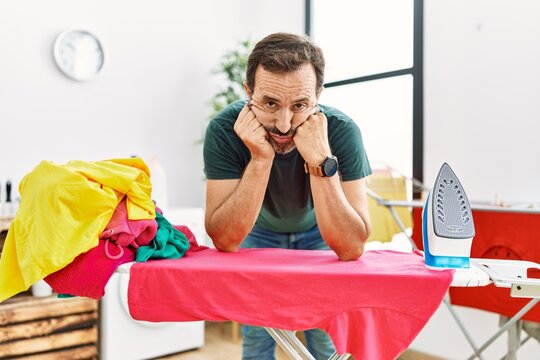 Middle Age Hispanic Man With Boring Expression Leaning On Iron Board At Home.