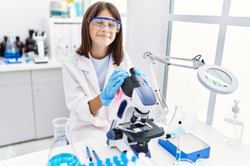 Young hispanic girl looking through microscope at laboratory