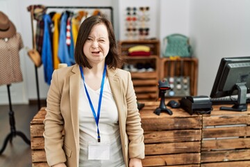 Young down syndrome woman working as manager at retail boutique winking looking at the camera with...