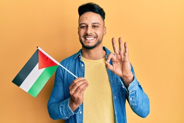 Young arab man holding palestine flag doing ok sign with fingers, smiling friendly gesturing...
