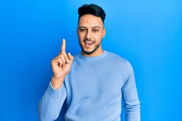 Fototapeta premium Young arab man wearing casual clothes smiling with an idea or question pointing finger up with happy face, number one
