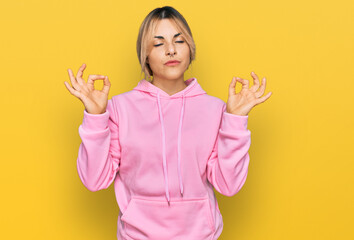 Young caucasian woman wearing casual sweatshirt relax and smiling with eyes closed doing meditation gesture with fingers. yoga concept.