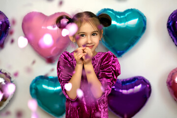 A girl on the background of bright colored foil balloons in the shape of a heart and flying...