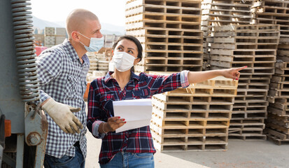 Manager in protective mask gives instructions to the car driver at the building materials storage...
