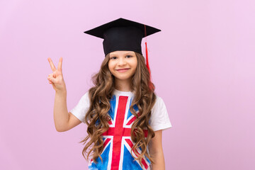 Portrait of a beautiful smiling schoolgirl in a master's cap and the flag of Great Britain on a...