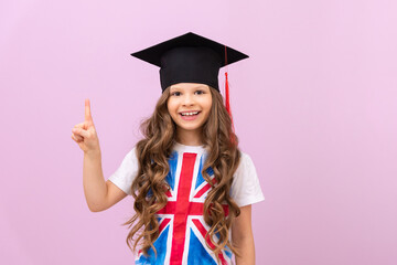 Portrait of a beautiful smiling schoolgirl in a master's cap and the flag of Great Britain on a T-shirt. English language courses, a schoolgirl points to the advertisement.