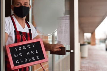 Diner restaurant owner holding Sorry We Are Closed sign due to pandemic lockdown