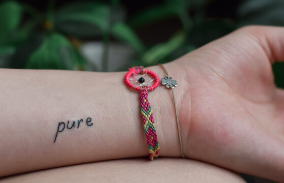 Closeup of young girl's hand with dreamcatcher bracelet and word Pure tattoo on arm