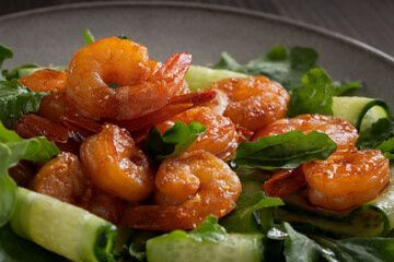 Fresh salad with grilled prawns, cucumbers and arugula, served on a plate, close-up