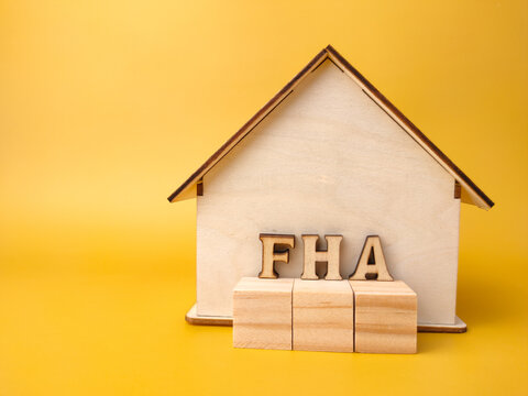 Wooden house and wooden block with word FHA on yellow background.