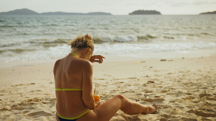 Lonely woman in swimwear on the beach drinks alcohol. Parting lo