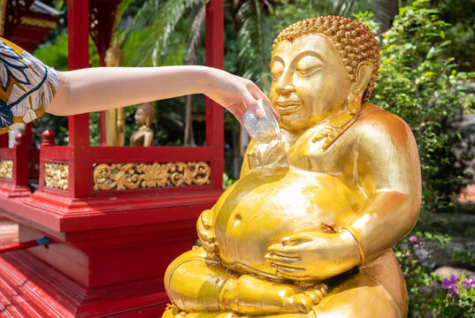 Woman hand pouring down scented water to fat Buddha statue during the Songkran festival in Thailand. This water festival marks the beginning of the traditional Thai New Year.