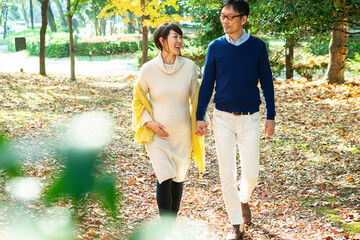 妊娠中の妻と手を繋いで、秋の公園を散歩する夫
