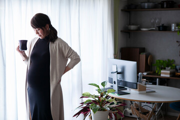 モーニングコーヒーを飲みながら窓辺に立つ、妊婦の女性