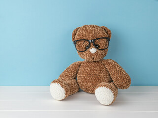 A beautiful knitted bear with glasses on a blue background.
