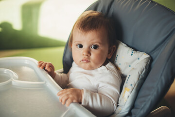 Portrait of a Caucasian baby girl sitting in high chair looking at camera, ready to eat. Baby care. Healthy lifestyle. Healthy food.