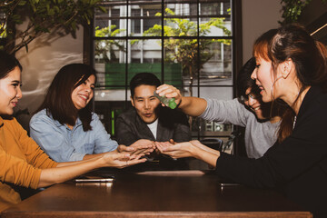 Group of colleagues, office workers, and businessmen sit together and playfully clean their hands using liquid alcohol gel to prevent tapeworms from COVID-19.