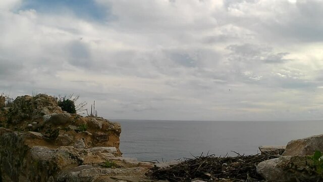 View from right to left of the broken stone roof walls of an old medieval fort of the blue sea on a cloudy day.