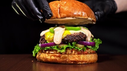 Craft burger is cooking on black background. Consist: sauce salsa, lettuce, red onion, pickle,...
