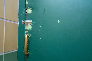 Old and worn green painted metal door with sliding bolt closure and brassy metal handle. 